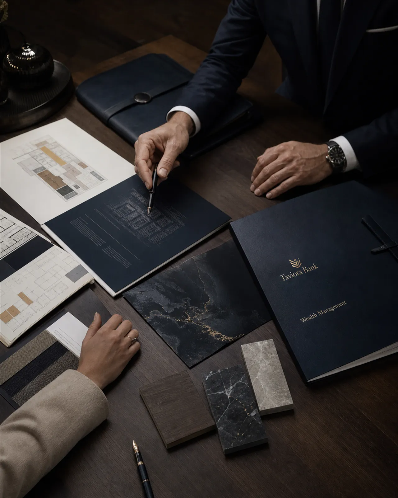 Wealth planning session — plans, material samples and a Taviora Wealth Management folio on a walnut table